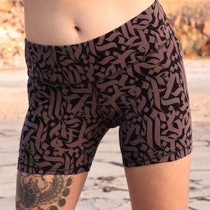 May include: Black and brown patterned athletic shorts. The shorts feature a repeating calligraphic design. The shorts are made of a stretchy material and are designed for athletic activities. The shorts are high-waisted and form-fitting.