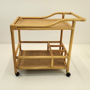 Op de afbeelding: Een bamboe barwagen met twee niveaus, met een geweven bovenste en onderste plank. De wagen heeft een handvat en wordt ondersteund door vier poten met kleine zwarte wielen. Het bamboe heeft een natuurlijke, lichtbruine kleur.