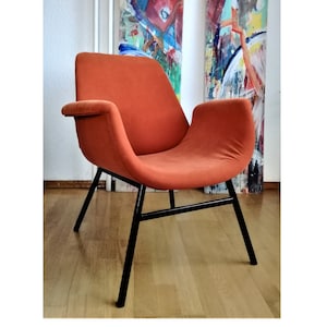 May include: A burnt orange armchair with black metal legs. The chair has a curved back and wide, rounded arms.