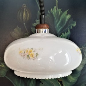 Op de afbeelding: Witte glazen hanglamp met een bloemenmotief. De lamp heeft een gegolfde rand en een houten bovenkant.