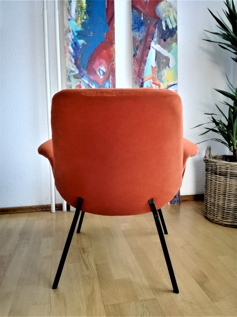 May include: A bright orange armchair with black metal legs. The chair is upholstered in a soft, plush fabric. The chair is sitting on a wooden floor.