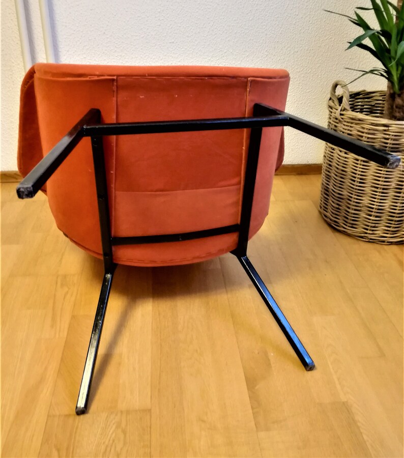 May include: A burnt orange armchair with a black metal frame. The chair is sitting on a wooden floor.