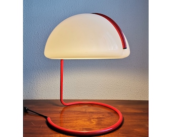 Puede incluir: Una lámpara de mesa roja y blanca con una base curva y una pantalla blanca. La lámpara está sobre una superficie de madera.