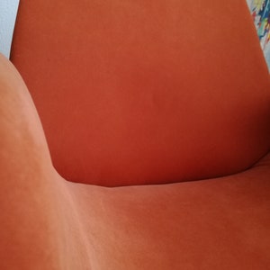 May include: A close-up of an orange-colored armchair with a curved back and seat. The chair is made of a soft, plush fabric.