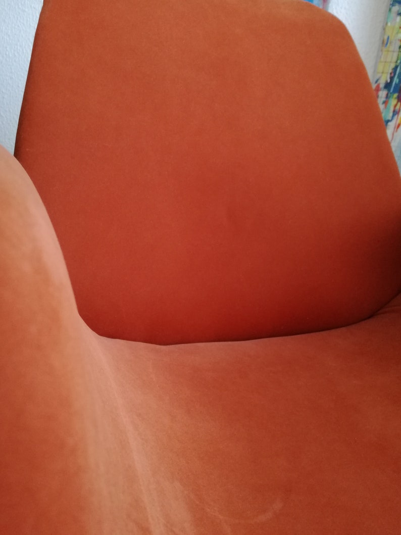 May include: A close-up of an orange-colored armchair with a curved back and seat. The chair is made of a soft, plush fabric.