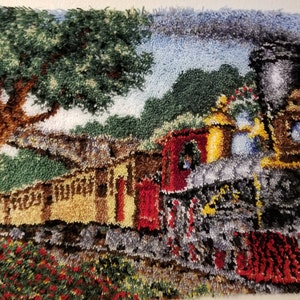 Puede incluir: Una alfombra colorida que representa un tren de vapor vintage viajando a través de un exuberante paisaje verde con un gran árbol a la izquierda y flores rojas en primer plano.