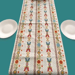Peut inclure: Un chemin de table blanc avec un motif floral coloré. Le motif présente des fleurs et des feuilles rouges, bleues, jaunes et vertes. Le chemin de table a un fond blanc avec un motif à pois subtil.