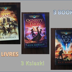Peut inclure: Trois livres brochés avec des couvertures colorées représentant des illustrations de personnes et de créatures mythologiques. Les titres sont "La Pyramide Rouge", "Le Trône de Feu" et "L'Ombre du Serpent" par Rick Riordan.