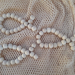 Könnte beinhalten: Drei Stränge aus Holzperlen in Form des Buchstabens "O" auf einem beigefarbenen Netz-Hintergrund.