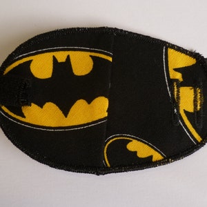 Może przedstawiać: Czarna maska na oczy z żółtym logo Batmana. Maska wykonana jest z miękkiej tkaniny i ma czarną gumkę.
