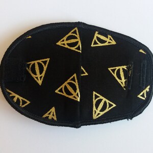May include: Black eye mask with a gold pattern of triangles with circles inside. The pattern is repeated across the mask.
