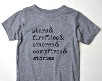 Op de afbeelding: Een grijs T-shirt met korte mouwen met de tekst "stars & fireflies & s'mores & campfires & stories" in zwart gedrukt.