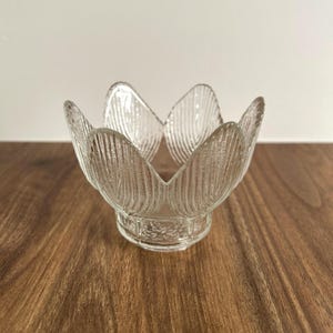Peut inclure: Un bol en verre transparent en forme de fleur ouverte avec six pétales distincts. Le verre présente un motif nervuré texturé sur l'extérieur de chaque pétale et une texture rugueuse et granuleuse autour de la base circulaire du récipient.