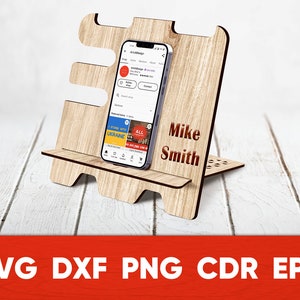 May include: A wooden phone stand with a personalized name, "Mike Smith", engraved on the front. The stand is designed to hold a smartphone upright, with a small shelf for the phone to rest on. The stand is made of light brown wood and has a natural wood finish.
