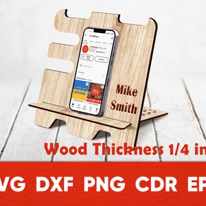 May include: A wooden phone stand with a personalized name "Mike Smith" engraved on the front. The stand is 1/4 inch thick and is designed to hold a smartphone in a vertical position. The stand is made of light brown wood and has a simple, modern design.