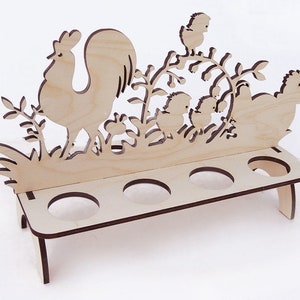 May include: Wooden egg holder with a rooster and chickens design. The holder has six slots for eggs and stands on two legs.