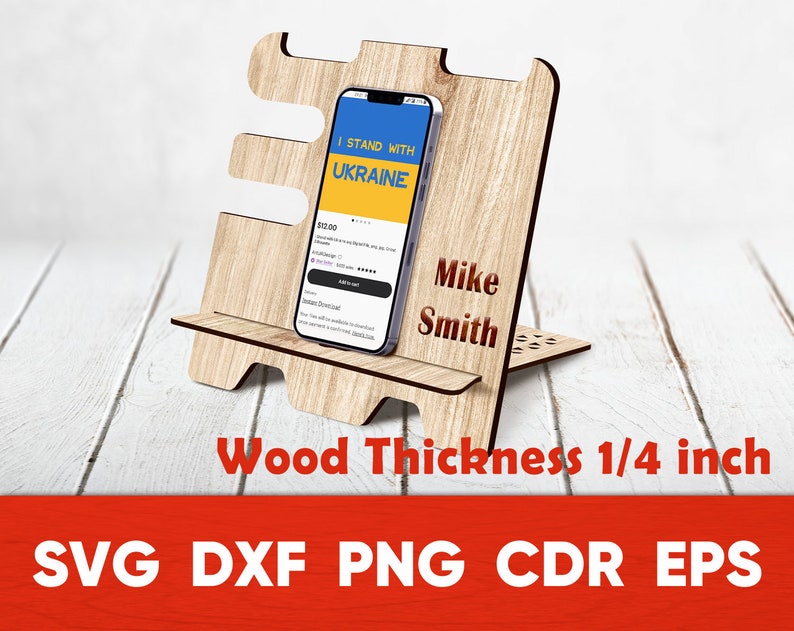 May include: A wooden phone stand with a cutout design. The stand is 1/4 inch thick and has a slot for a phone. The phone in the stand displays the text "I Stand With Ukraine". The stand is personalized with the name "Mike Smith".