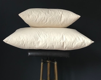May include: Two white cotton pillows stacked on top of each other on a gold metal stand against a dark blue background.