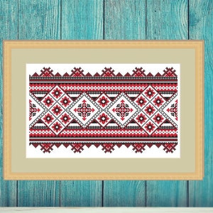 Könnte beinhalten: Ein gerahmtes Kunstwerk mit einem traditionellen geometrischen Muster in Rot, Schwarz und Weiß. Das Kunstwerk wird auf einer weißen Oberfläche vor einem türkisfarbenen Holzhintergrund präsentiert. Eine weiße Vase befindet sich im Vordergrund.