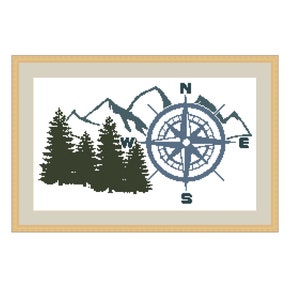 May include: Cross-stitch artwork in a wooden frame. The design shows a compass rose, mountains, and evergreen trees in blue and green. The compass points are labelled N, E, S, and W.
