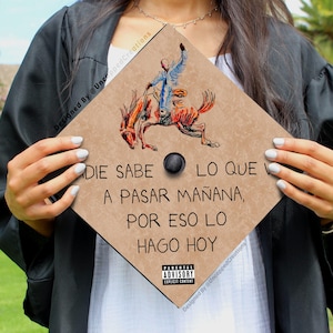 May include: A brown graduation cap with a cowboy riding a horse illustration. The cap has the text "Nadie sabe lo que va a pasar ma&ntilde;ana, por eso lo hago hoy" printed on it.