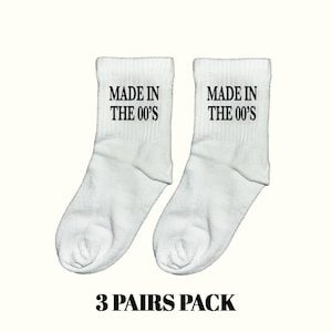 Pode incluir: Dois pares de meias brancas com o texto "MADE IN THE 00'S" em preto. A imagem também inclui o texto "3 PAIRS PACK" em preto.