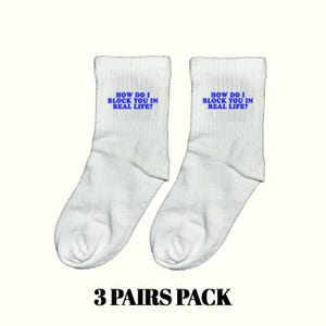 Könnte beinhalten: Zwei weiße Socken mit dem blauen Text "HOW DO I BLOCK YOU IN REAL LIFE?". Das Bild enthält auch den schwarzen Text "3 PAIRS PACK".