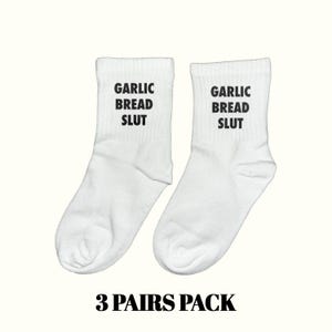 May include: Two white crew socks with the text "GARLIC BREAD SLUT" printed in black. The socks are displayed on a light background. The text "3 PAIRS PACK" is printed in black at the bottom.