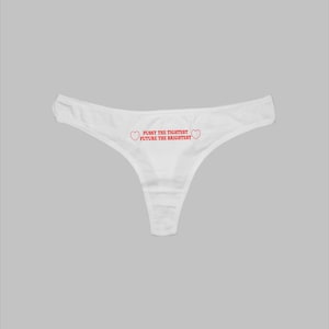 May include: White thong underwear featuring the red text "PUSSY THE TIGHTEST FUTURE THE BRIGHTEST" with a heart on either side. The underwear is displayed against a light grey backdrop.