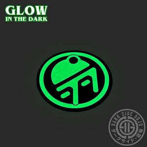 May include: A circular patch featuring a black background with a bright green glowing graphic design. The text GLOW IN THE DARK appears in green at the top left, and a circular logo with the text DARK SIDE DOJO is in the bottom right corner.
