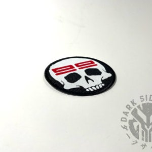 May include: White skull with red and black stripes across the forehead. The skull is embroidered on a black circular patch.