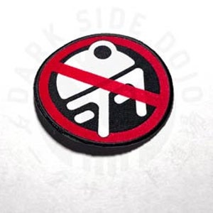 May include: A red circle with a diagonal line through it. Inside the circle is a white silhouette of a droid with a red line through it. The circle is black with a red border.