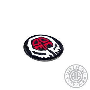 May include: A black, white, and red patch featuring a stylized skull design. The patch has a circular shape with the words "DARK SIDE DOJO" in a circular logo on the bottom right.