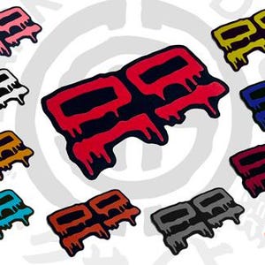 May include: A collection of eleven stickers featuring a stylized double-square logo with a dripping paint effect in various colors including red, pink, white, yellow, blue, orange, teal, maroon, and gray, with a Dark Side Dojo logo in the corner.