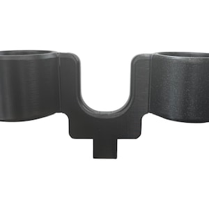 May include: A black plastic double cup holder with a U-shaped design. The holder has two circular openings for cups.