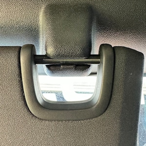 May include: A black sun visor clip with a metal bar and a textured surface.