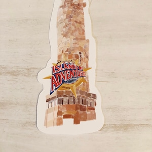 May include: A sticker featuring a tall, brown lighthouse with a detailed brick pattern. The lighthouse has a dark top and the words "ISLANDS OF ADVENTURE" in red and blue, with a compass rose design.