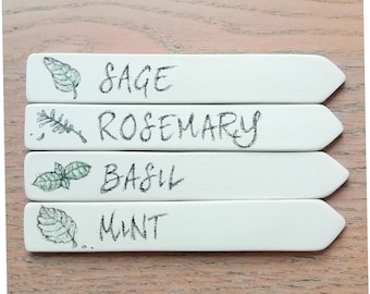 Op de afbeelding: Vier witte rechthoekige tuinmarkeringen met puntige uiteinden. Elke markering heeft een andere kruidnaam in het zwart geschreven: Salie, Rozemarijn, Basilicum en Munt. Elke markering heeft ook een bijbehorende groene illustratie van het kruid.