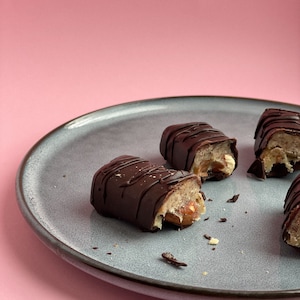 Könnte beinhalten: Vier karamellgefüllte Schokoladenbonbons auf einem grauen Teller. Die Bonbons sind in einem Halbkreis angeordnet, wobei ein Bonbon in zwei Hälften gebrochen ist und die Karamellfüllung sichtbar wird.