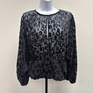May include: A black blouse with a leopard print design. The long-sleeved top has a round neckline and a small opening at the chest. The fabric has a sheer quality, and the leopard spots are in a darker shade of black and blue.