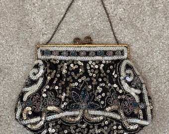 May include: A vintage black beaded handbag with a gold frame and chain handle. The bag is covered in sequins and features floral and scrollwork designs in gold, white, and blue. The bag measures approximately 20 cm wide.