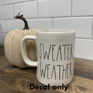 May include: A white ceramic mug with the words "SWEATER WEATHER" in black lettering. A decorative beige pumpkin with a brown stem sits behind the mug. The words "Decal only" are at the bottom.