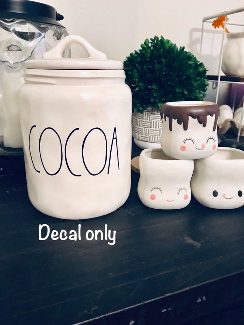 May include: White ceramic cocoa jar with black lettering that says "COCOA".  The jar has a lid with a handle.  There are three white ceramic mugs with brown chocolate glaze and a smiling marshmallow face.  The text "Decal only" is written below the jar.