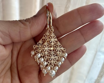 Peut inclure: Boucles d'oreilles pendantes dorées avec un motif filigrané délicat et un groupe de perles blanches suspendues au bas.