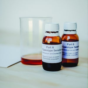 Peut inclure: Deux flacons en verre ambr&eacute; avec des bouchons blancs et des &eacute;tiquettes. Les &eacute;tiquettes indiquent "Part A Cyanotype Sensitiser Ammonium and Distilled Water Keep out of reach of children Not for human consumption" et "Part B Cyanotype Sensitiser Ferricyanide and Distilled Water Keep out of reach of children Not for human consumption".