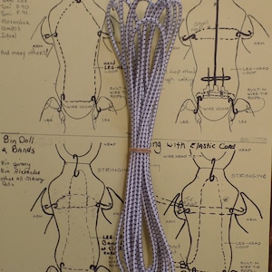 May include: White elastic string with black dots, used for stringing dolls. The string is shown next to a diagram of a doll with instructions for stringing it. The text on the diagram reads "Whisker Dolls" and "Bin Doll 2 Bands".