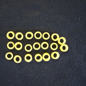 May include: A row of 20 yellow rubber bands arranged in a line on a dark blue surface.