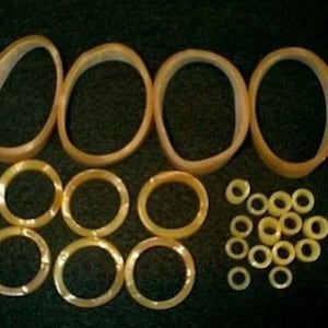 May include: A collection of beige rubber bands in various sizes. The rubber bands are arranged in a circle with the smaller bands in the center.