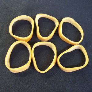 May include: Six tan-colored rubber bands arranged on a dark blue surface. The rubber bands are oval-shaped and appear to be new. The image is a close-up shot, highlighting the texture and color of the rubber bands.