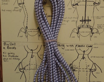 May include: A close-up of a white elastic cord with black stripes. The cord is coiled and ready to be used for stringing dolls. The image also includes a diagram of a doll with instructions for stringing it.